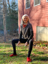 Woman sitting on a birth stool outdoors in front of a red building.