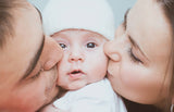 Two adults kissing a baby on each cheek, with a light blue background